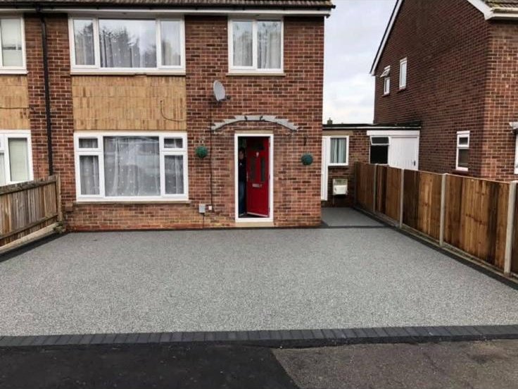 Wide silver resin bound driveway with charcoal block edging on a semi-detached home